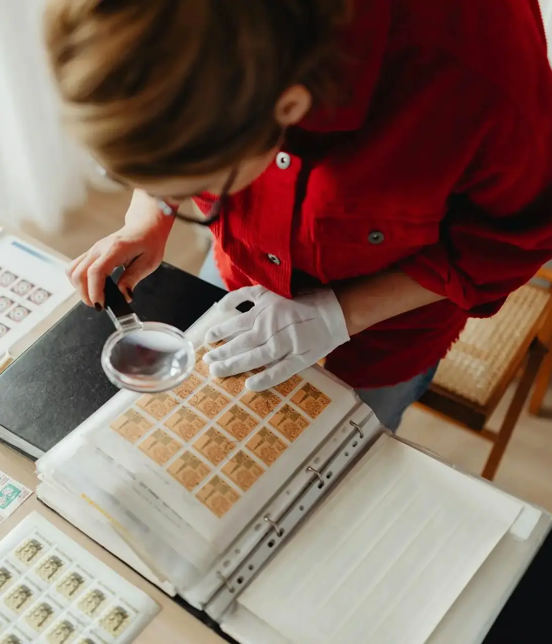 Vintage Stamp Collection Appraisals – Expert Valuation & Estate Sales Person carefully inspecting a vintage stamp collection with a magnifying glass, symbolizing expert appraisal and authentication services.
