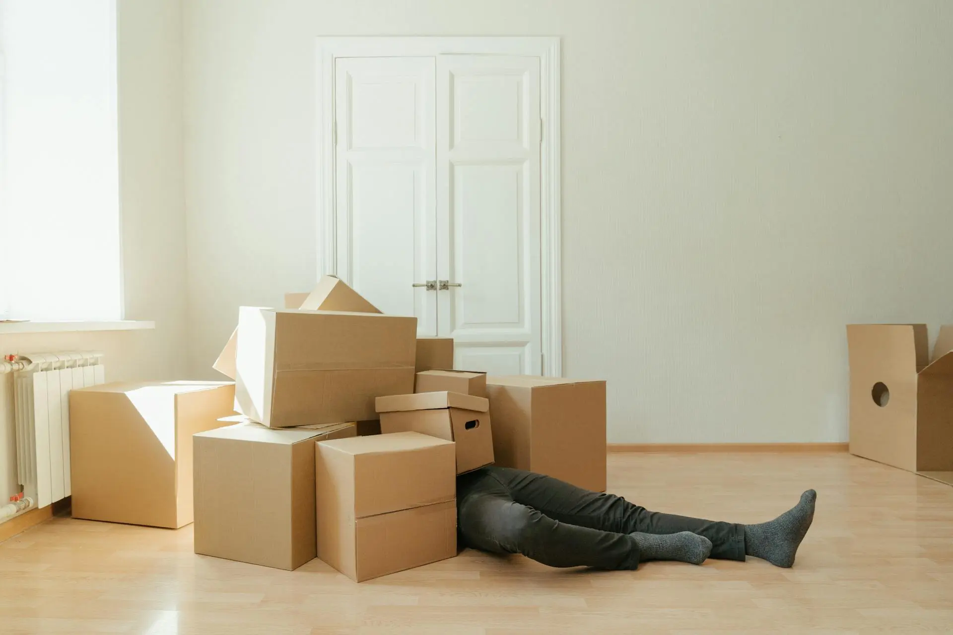 Overwhelmed person buried under a stack of moving storage boxes, symbolizing the challenges of estate cleanouts and downsizing.